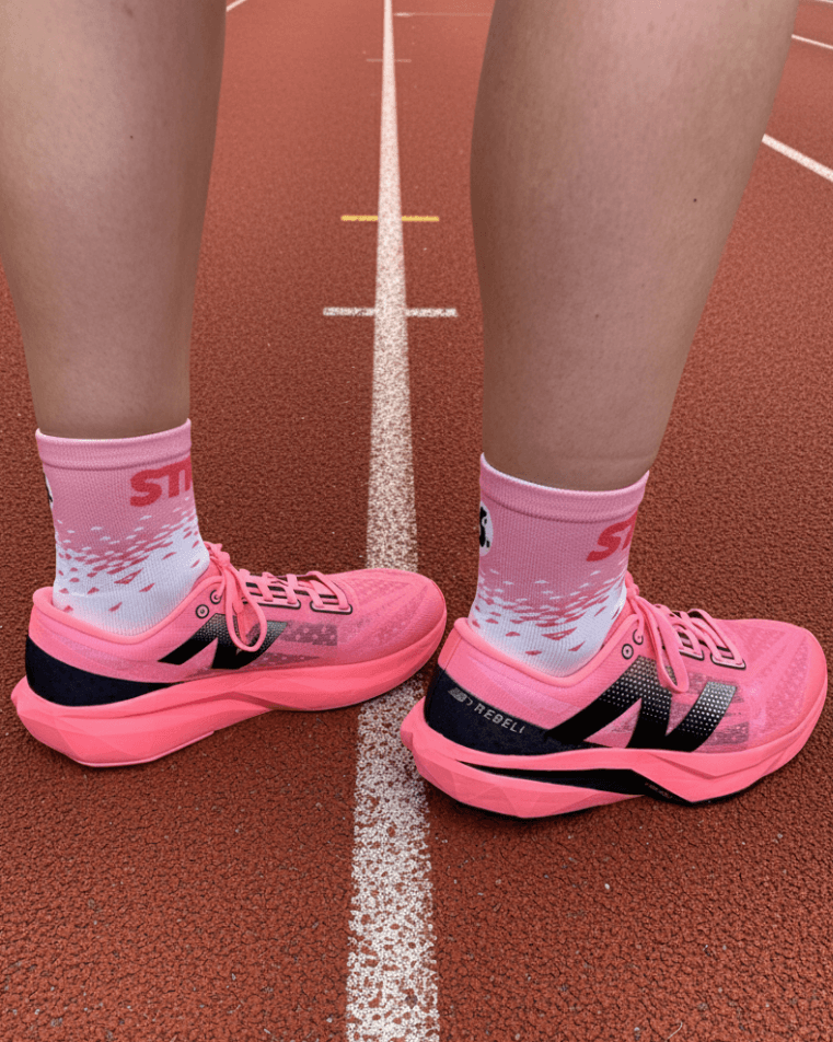 A close-up of a person's feet wearing pink running shoes and matching socks on a track.