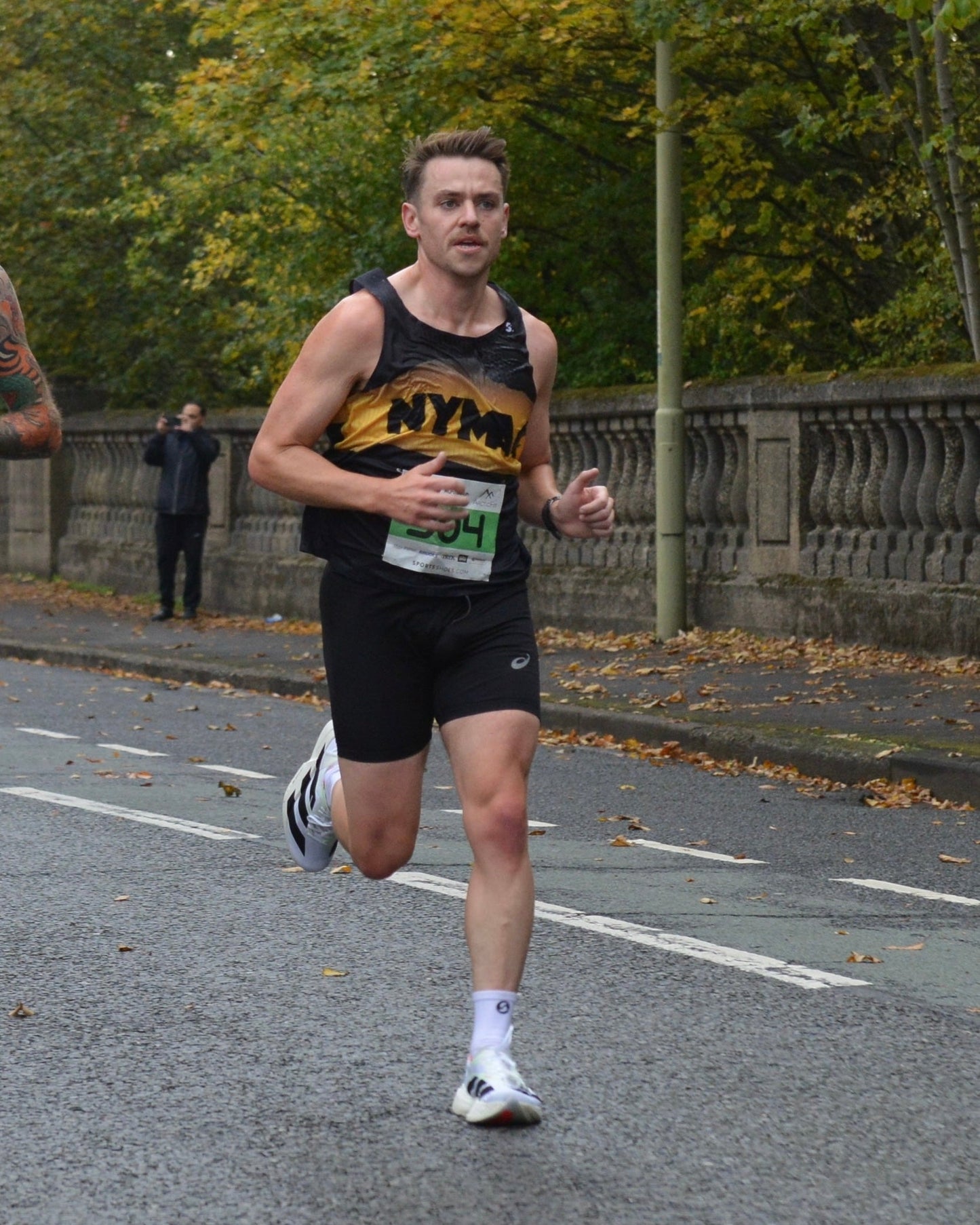 Runner in a black and yellow athletic vest during a race on a paved road.