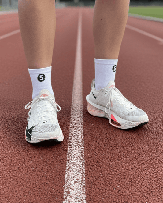 A person's legs and feet wearing white athletic socks and running shoes on a track.