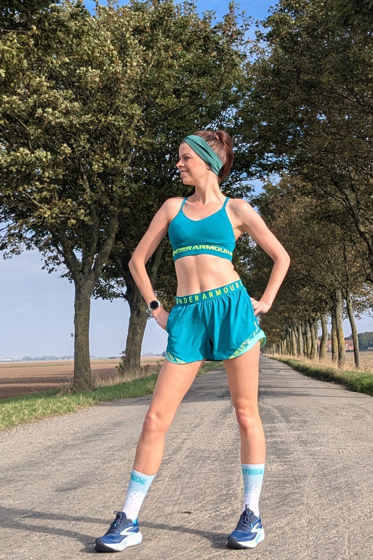 Person in athletic wear standing on a road with trees and open sky in the background