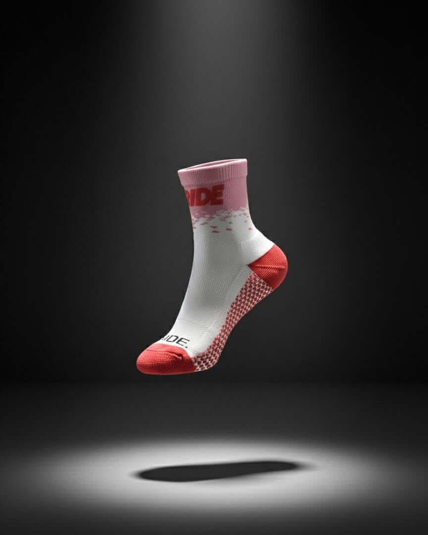 A white, pink, and red cycling sock floats against a dark background, spotlit from below.