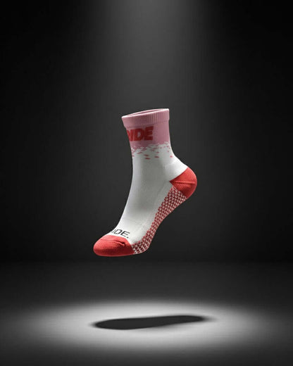 A white, pink, and red cycling sock floats against a dark background, spotlit from below.