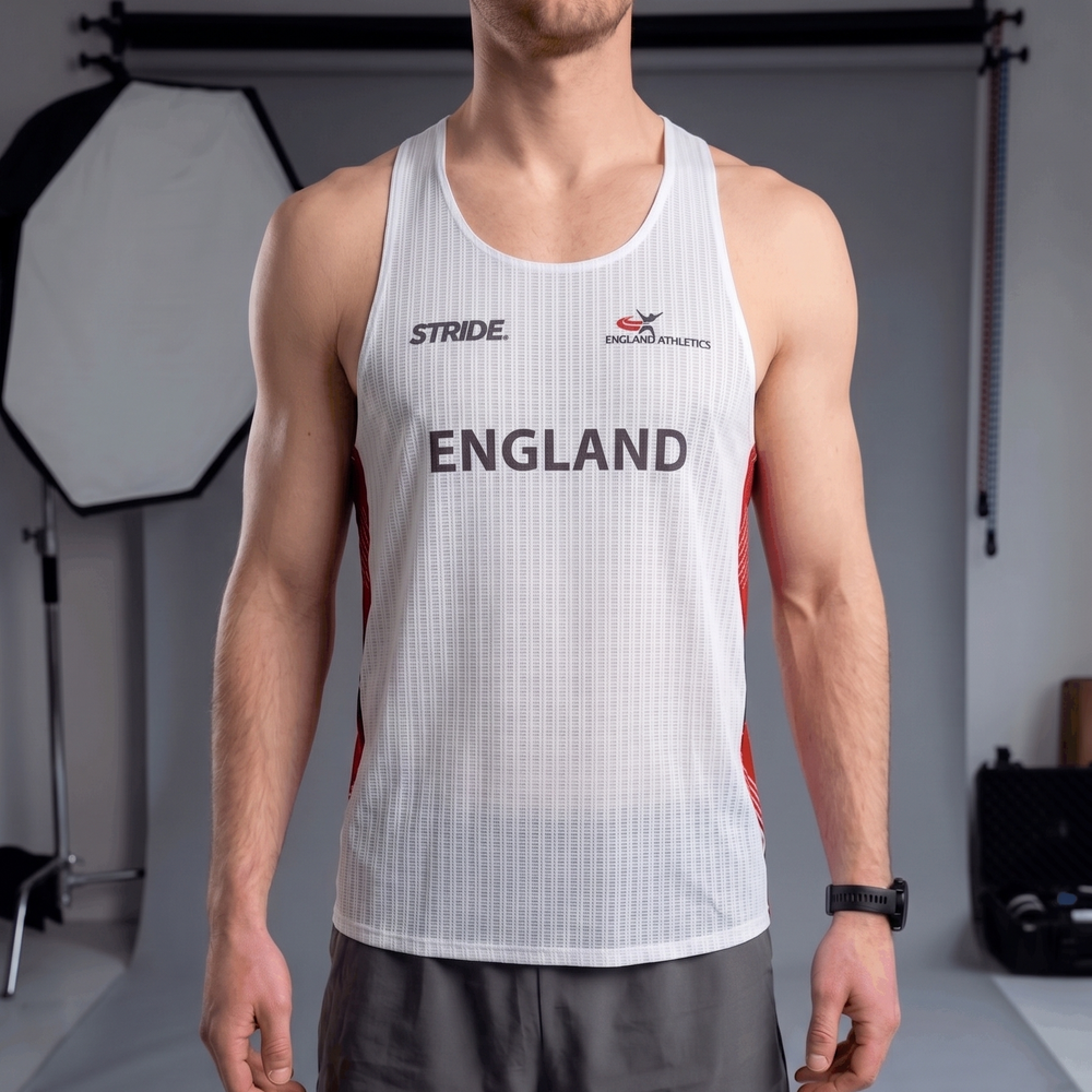 Person wearing a white tank top with 'England' printed on it, standing in a studio setting.