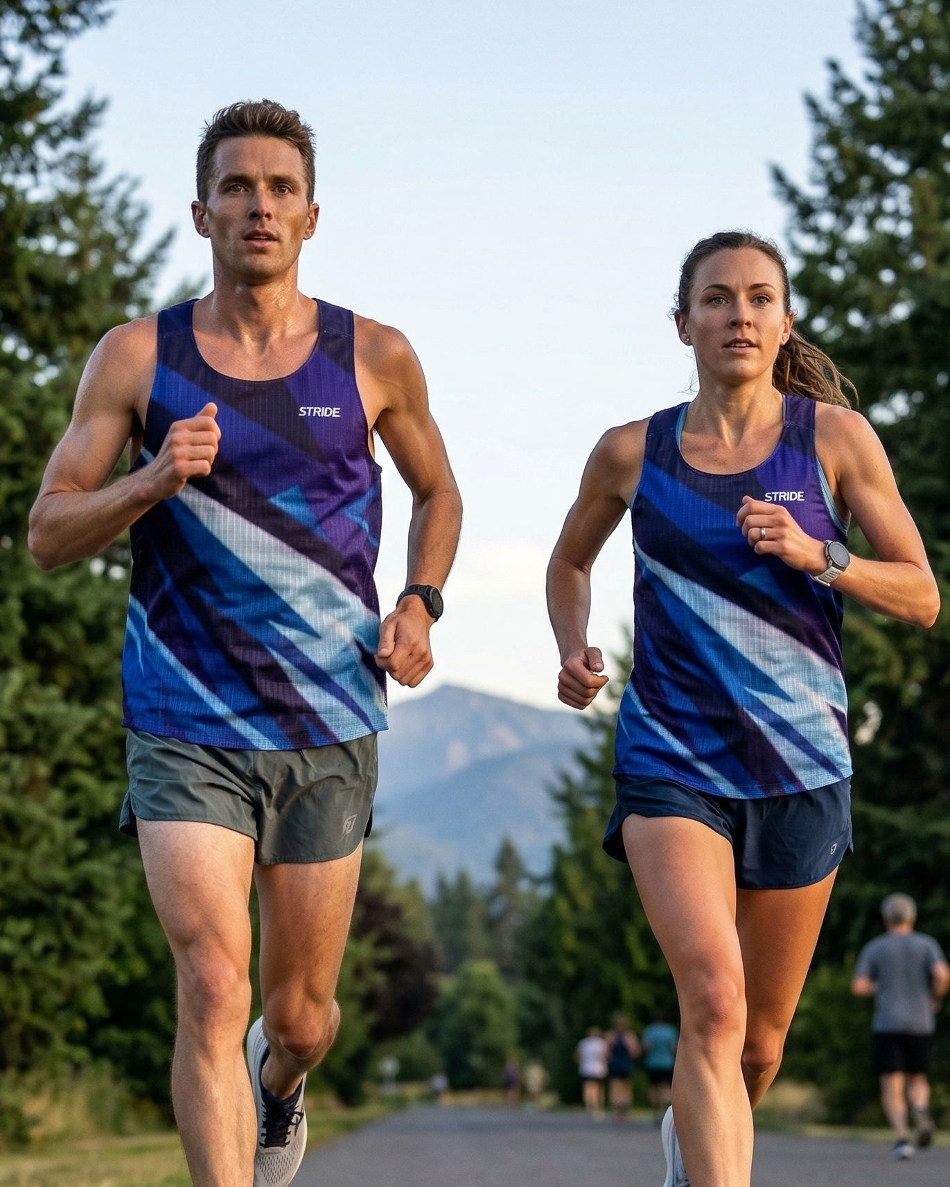 Two runners in matching athletic outfits running on a path with trees and mountains in the background.
