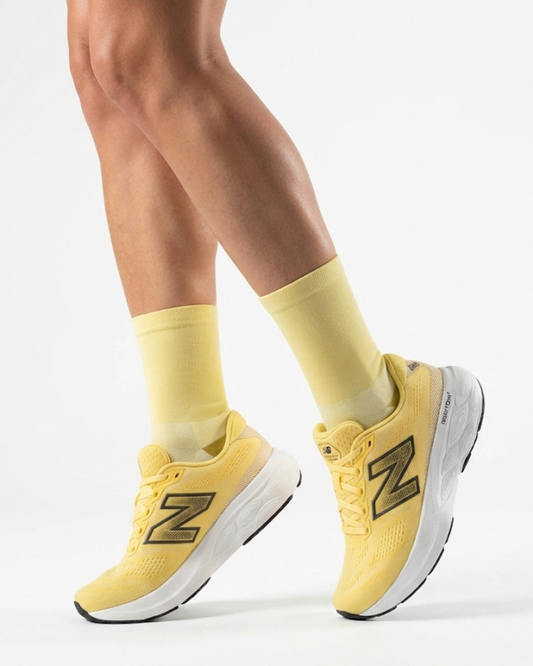 Yellow running shoes with a brand logo worn with matching socks on a light background